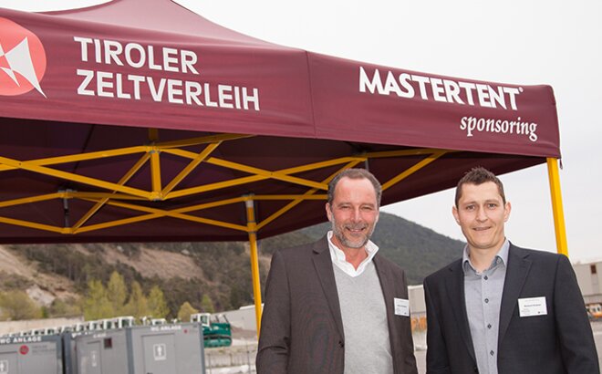 Die beiden Geschäftsführer posieren mit einem Lächeln vor einem Faltpavillon vom Tiroler Zeltverleih mit MASTERTENT Sponsering