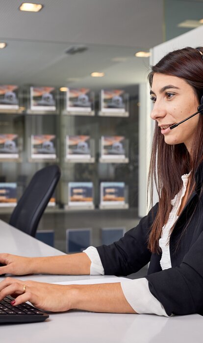 Un angajat stă în fața PC-ului cu o cască și oferă asistență clientului la telefon.
