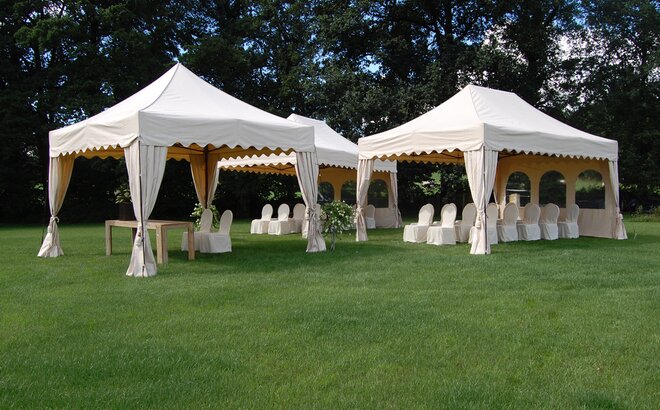 Three white gazebos are standing in the meadow. Underneath the gazebos are chairs with overcoat. 