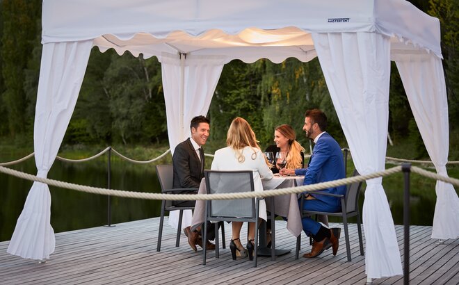 Die 4 Gäste sitzen unter dem Faltpavillon beim Abendessen.