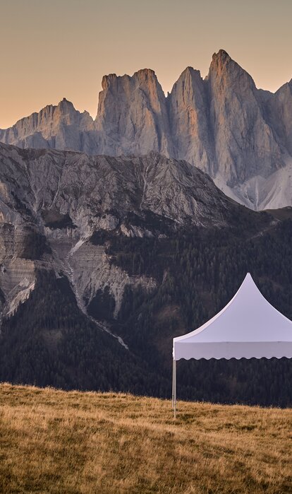 Das weiße Pagodenzelt steht am Berg. Dahinter erstreckt sich eine traumhafte Bergkette im Sonnenuntergang.