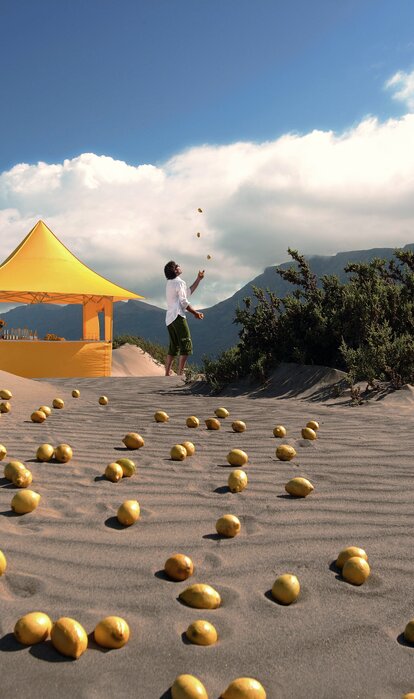Gelber Faltpavillon der Größe 3x3 m mit Vordach und verschiedenen Seitenwänden auf sandigem Untergrund inmitten der Wüste. Ein Mann jongliert neben dem Faltzelt.