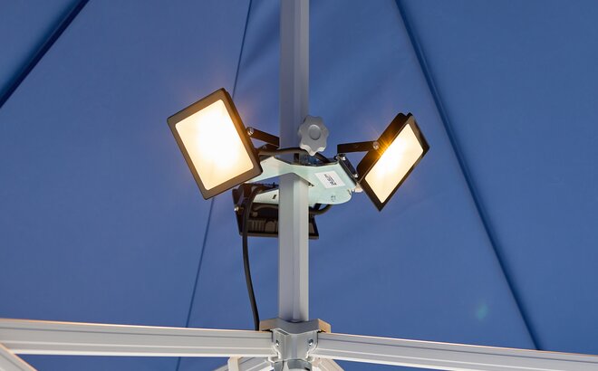 Tre faretti LED sono montati sul gazebo pieghevole blu. I riflettori a LED sono tutti accesi.