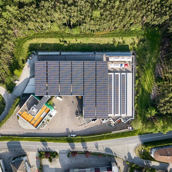 An overhead shot of the Zingerle Group production facility showing solar panels on the roof. The building is surrounded by trees.