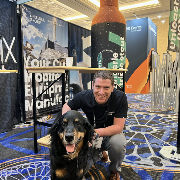 A man kneeling next to a dog under a tent at a marketing tradeshow.