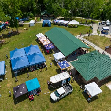 An aerial shot of many canopy tents set up on a waterfront park for an event.