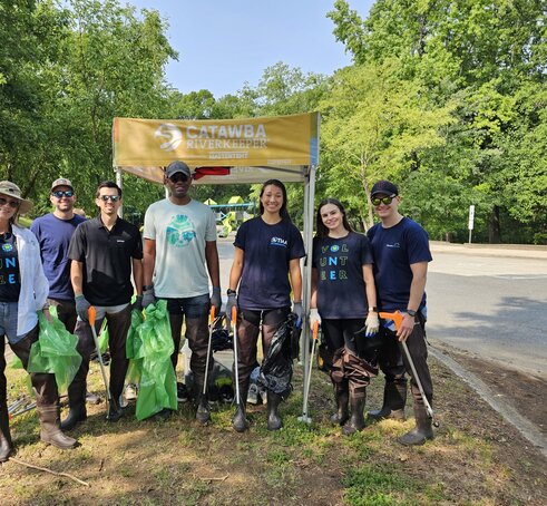 Participants of an outdoor cleanup stand in front of a 5x5 custom canopy tent. 