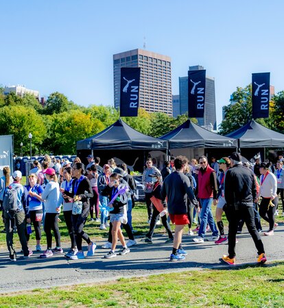 Black Mastertent 10x10ft canopy tents set up in a row with peak flags printed with Puma logos. Surrounded by crowd of people for a post-race event.