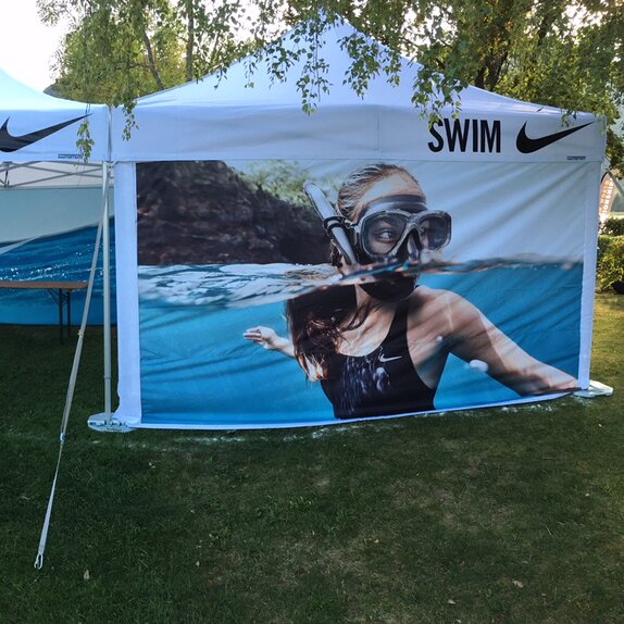 Auf dem Bild sind weiße Faltpavillons von Nike in den Größen 6x4m und 4x4m mit individuell gestalteten Seitenwänden zu sehen. Außerdem sind sie mit dem Nike Swim Logo bedruckt.