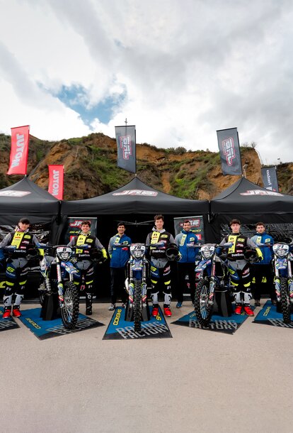 Auf dem Bild sind drei schwarze Faltpavillons mit Fahnen zu sehen. Die Zelte sind mit dem Logo des Motorradteams bedruckt. Das Team steht vor den Zelten.