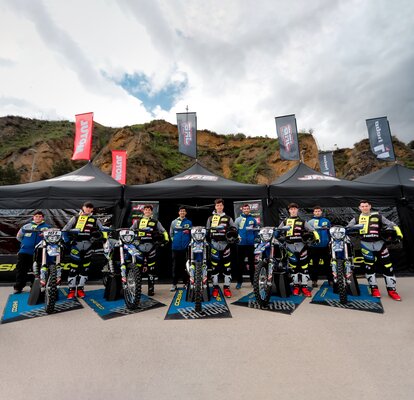 Auf dem Bild sind drei schwarze Faltpavillons mit Fahnen zu sehen. Die Zelte sind mit dem Logo des Motorradteams bedruckt. Das Team steht vor den Zelten.