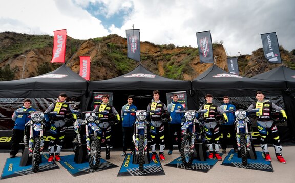 Auf dem Bild sind drei schwarze Faltpavillons mit Fahnen zu sehen. Die Zelte sind mit dem Logo des Motorradteams bedruckt. Das Team steht vor den Zelten.