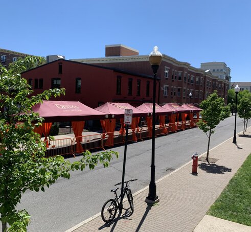 A row of Mastertent Series 1 20x10 canopy tents arranged in a multi-tent system for outdoor dining. Bordeaux roof and orange corner curtains branded for Delta's Restaurant.