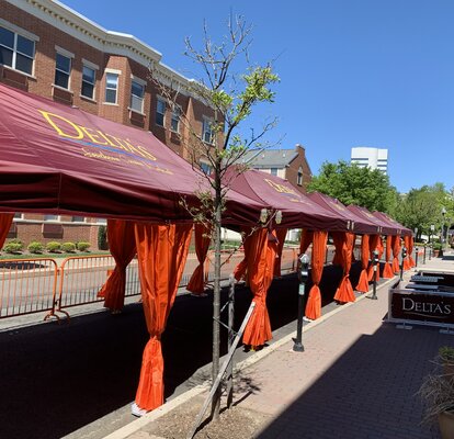 A row of Mastertent Series 1 20x10 canopy tents arranged in a multi-tent system for outdoor dining. Bordeaux roof and orange corner curtains branded for Delta's Restaurant.