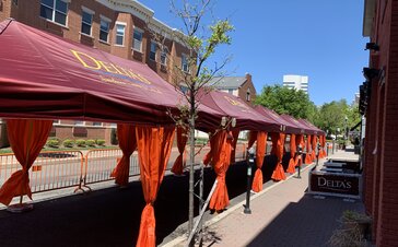 A row of Mastertent Series 1 20x10 canopy tents arranged in a multi-tent system for outdoor dining. Bordeaux roof and orange corner curtains branded for Delta's Restaurant.