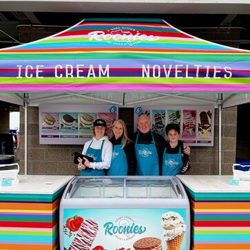 A bright, colorful printed tent over an ice cream serving station. Roonie's Ice Cream owners and family underneath.