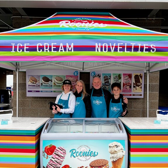 A bright, colorful printed tent over an ice cream serving station. Roonie's Ice Cream owners and family underneath.