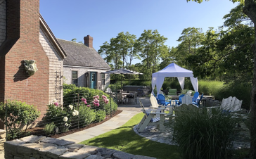A white canopy tent with elegant corner curtains in a private backyard garden.