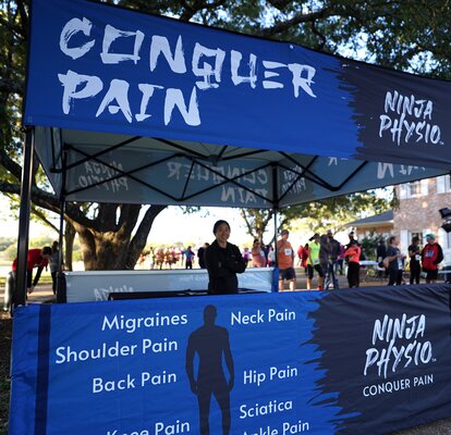 A Mastertent Square 10x10 canopy tent printed in black and blue as an information booth for Ninja Physio chiropractic care. 