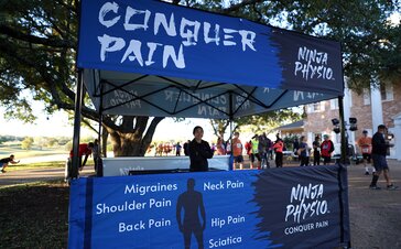 A Mastertent Square 10x10 canopy tent printed in black and blue as an information booth for Ninja Physio chiropractic care. 