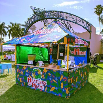 A Mastertent folding gazebo printed with colourful patterns with an awning and with a counter to serve food.