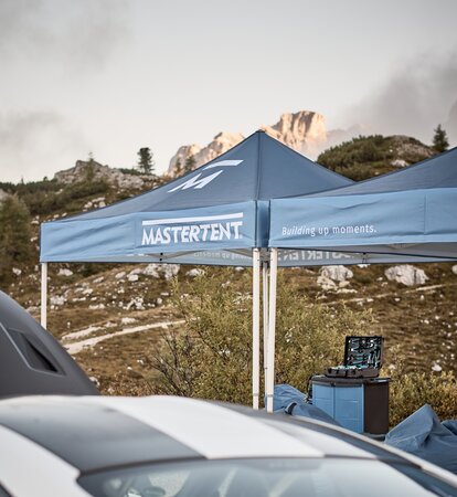 Blue printed canopy tents with Mastertent logos set up with mountains in the background.