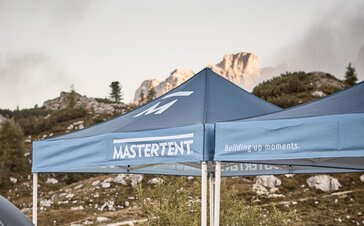 Blue printed canopy tents with Mastertent logos set up with mountains in the background.