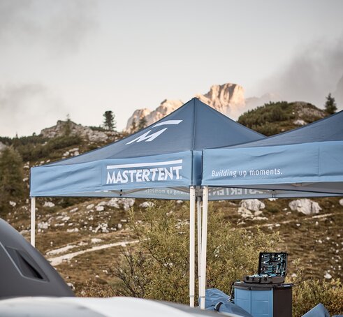 Blue printed canopy tents with Mastertent logos set up with mountains in the background.
