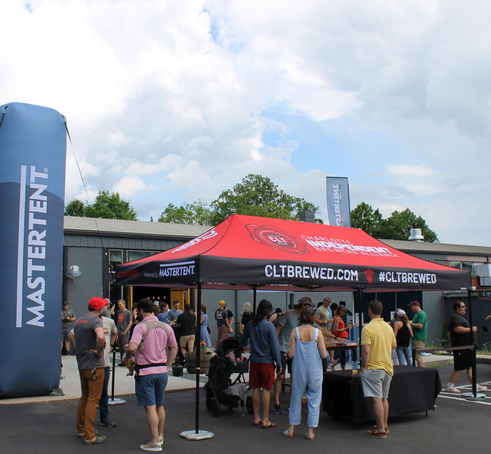 Posed next to a custom event inflatable, a custom 20x10 event tent shades event goers as they taste different beers from breweries. This tent has a custom colored tent frame and custom printing. 