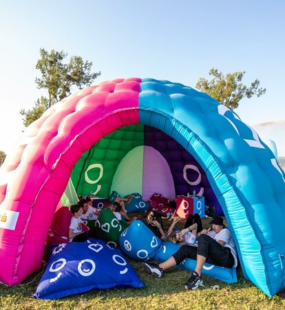 A multi-color dome inflatable advertising structure set up in a park for an event.