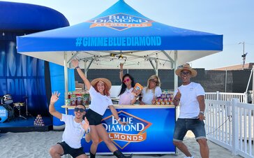 Crowd pose for picture on the sand under Blue Diamond branded Mastertent square pavilion.