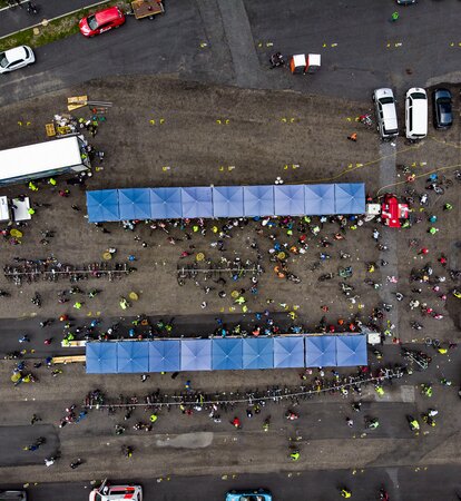 Two lines of nine square, blue Mastertent canopy tents on asphalt seen from above with people and cars crowded around.
