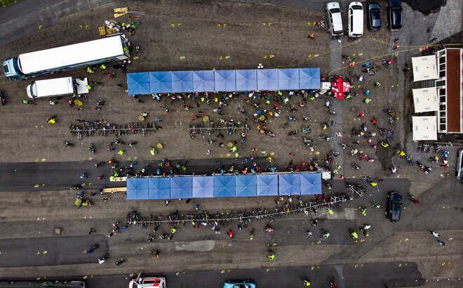 Two lines of nine square, blue Mastertent canopy tents on asphalt seen from above with people and cars crowded around.