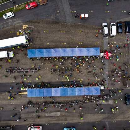 Two lines of nine square, blue Mastertent canopy tents on asphalt seen from above with people and cars crowded around.