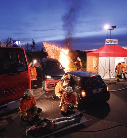 Firefighters on scene of accident with trucks, medical tent, and spotlights