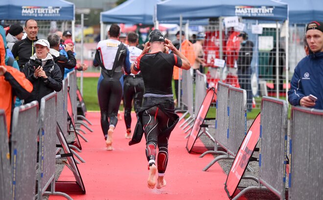 Three men in swim body suits running away from camera in triathlon with fans crowded on either side