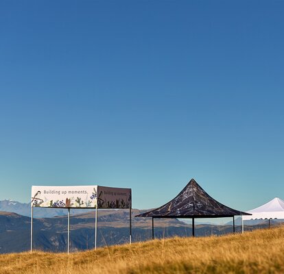 4 canopy tents with different style roofs lined up diagonally in a field with sunny blue sky. 