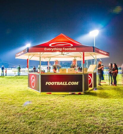 Red pavilion for football club on green football field with blurred people in crowd at night