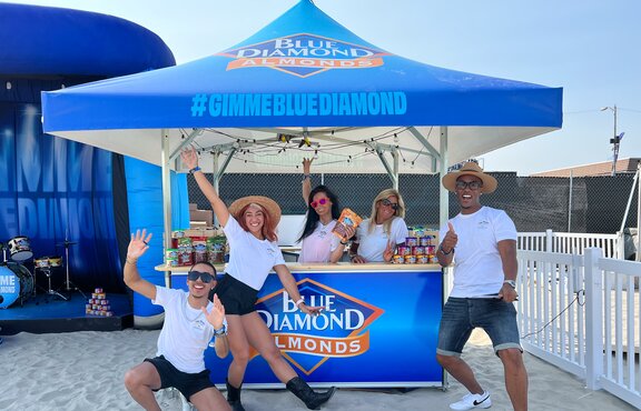 Crowd pose for picture on the sand under Blue Diamond branded Mastertent square pavilion.