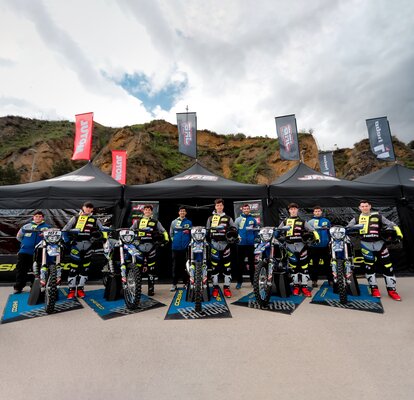 Nella foto ci sono tre gazebo pieghevoli neri con bandiere. I gazebo sono personalizzati con il logo del team di motociclisti. I motociclisti e le loro moto stanndo davanti ai gazebo.