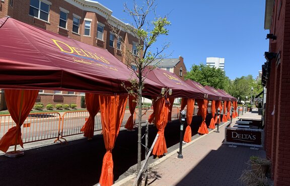 A row of Mastertent Series 1 20x10 canopy tents arranged in a multi-tent system for outdoor dining. Bordeaux roof and orange corner curtains branded for Delta's Restaurant.