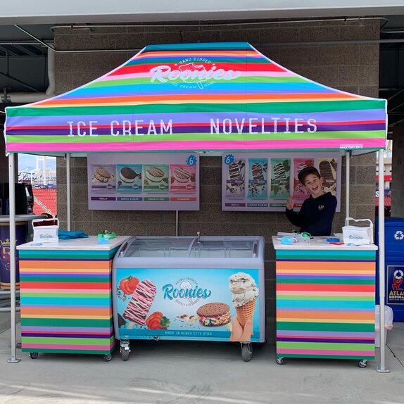 A bright, colorful printed tent over an ice cream serving station. Roonie's Ice Cream owners and family underneath.