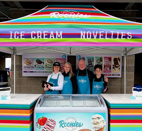 A bright, colorful printed tent over an ice cream serving station. Roonie's Ice Cream owners and family underneath.