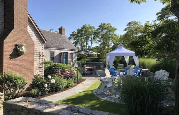 A white canopy tent with elegant corner curtains in a private backyard garden.