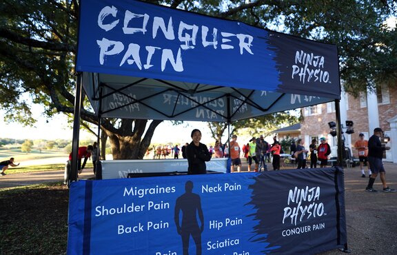 A Mastertent Square 10x10 canopy tent printed in black and blue as an information booth for Ninja Physio chiropractic care. 