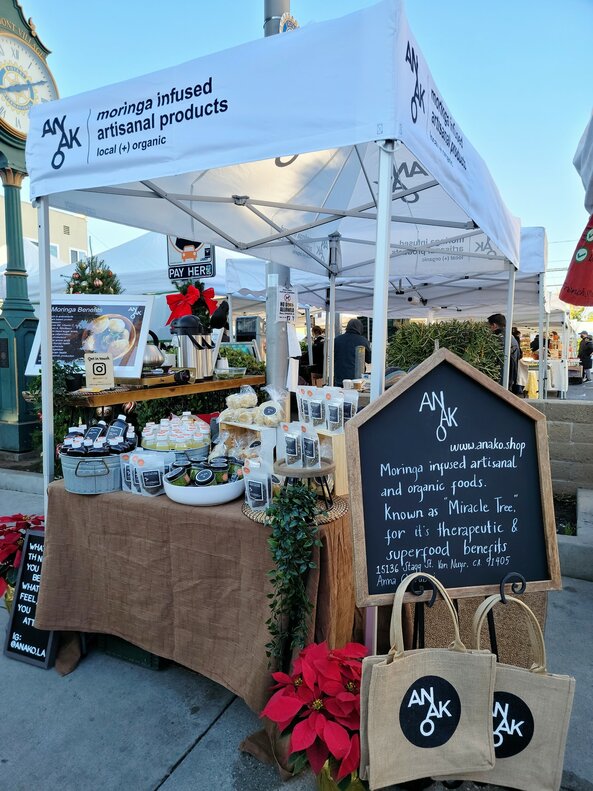A white 10x5ft Mastertent canopy tent set up at a market to sell Anako moringa infused products at a farmer's market.