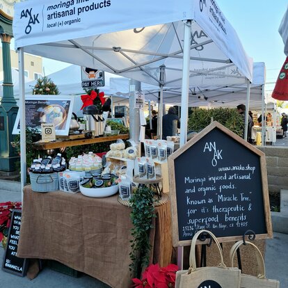 A white 10x5ft Mastertent canopy tent set up at a market to sell Anako moringa infused products at a farmer's market.