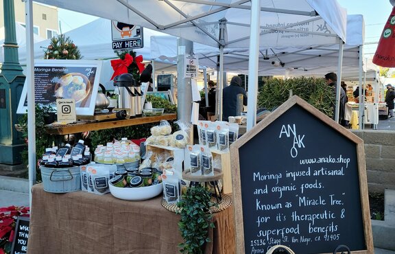 A white 10x5ft Mastertent canopy tent set up at a market to sell Anako moringa infused products at a farmer's market.