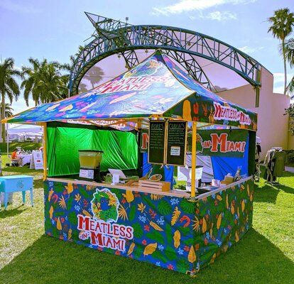 A Mastertent canopy tent printed with bright colorful patterns with counters to serve food.