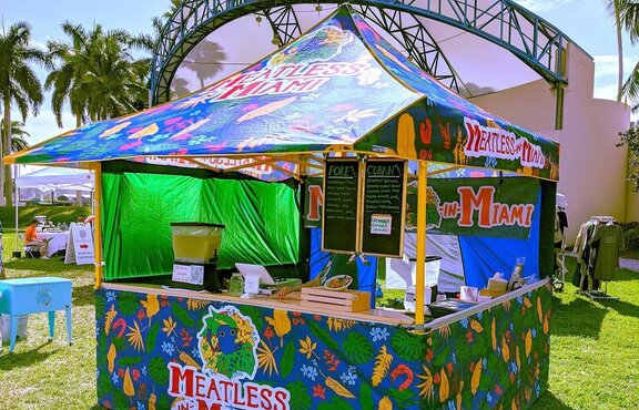A Mastertent folding gazebo printed with colourful patterns with an awning and with a counter to serve food.